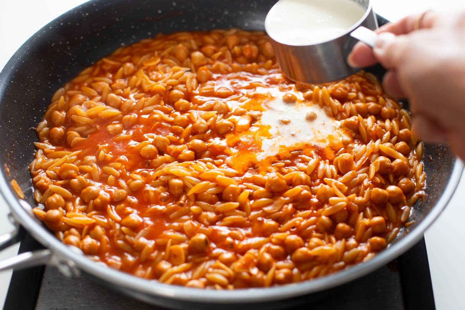 Adding heavy cream to a skillet with orzo and chickpeas.