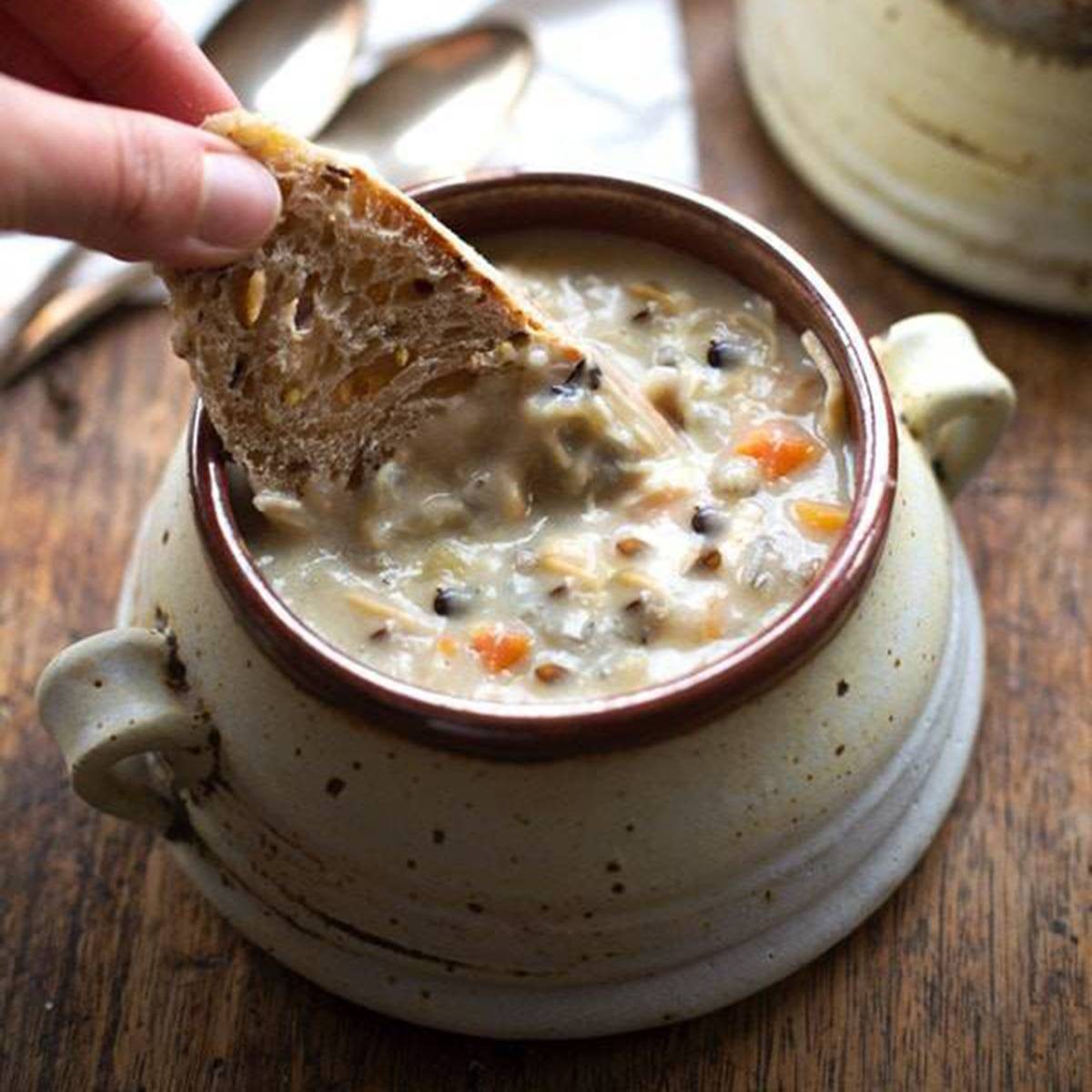 White hand dunking bread into chicken wild rice soup