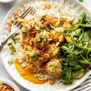 Yellow curry meatballs on a plate with rice and greens.