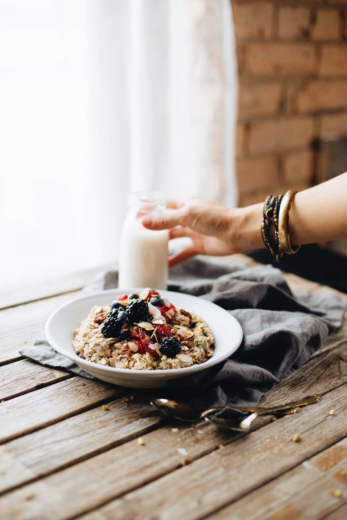 Hand grabbing a glass of milk next to a plate of granola with berries.