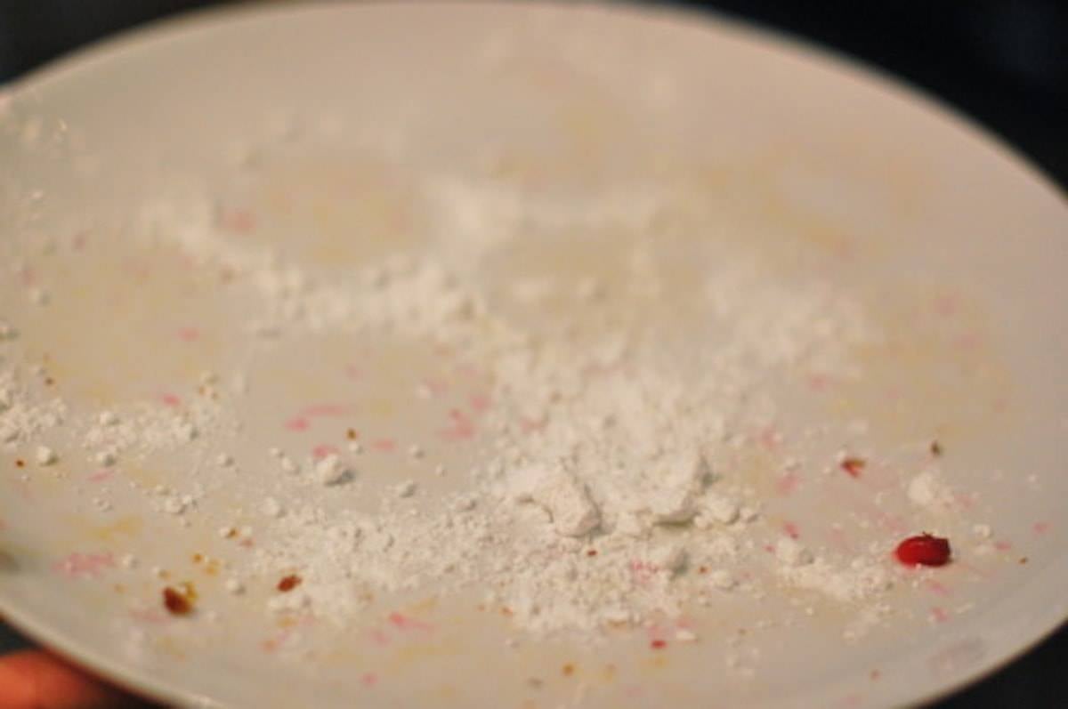 White plate with muffin remains including pomegranate seeds and powdered sugar.